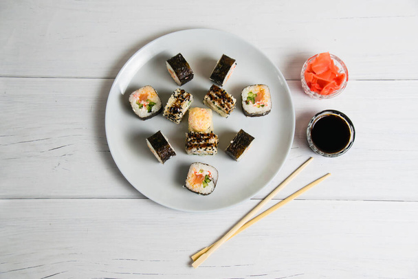 Sushi-Rollen auf einem Teller auf hellgrauem Hintergrund, Bambusstäbchen, Sojasauce und Ingwer, flache Lage, Kopierraum. - Foto, Bild