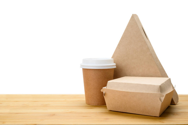 Lunch food delivery concept. Set of paper containers (pizza, hamburger, coffee paper cup) on a wooden table. Isolated background. - Photo, Image