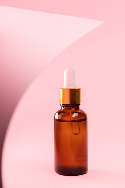 Close up of brown glass cosmetic bottle with dropper on a pink background with abstract decor. The concept of an advertising template for beauty products. - Fotoğraf, Görsel