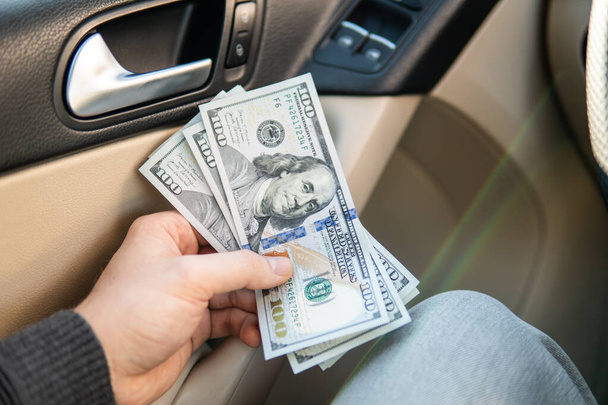 Closeup holding dollar bills in car dealership background. Personal transportation purchase concept money - Φωτογραφία, εικόνα