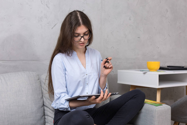 Una giovane designer seduta su un divano disegna su un tablet. Fa calcoli di affari sul computer. - Foto, immagini