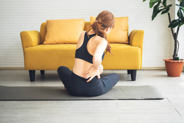 Азиатская привлекательная молодая женщина, в настоящее время испытывает боли в пояснице во время упражнений в домашних условиях, из-за остеоартрита, в спорте и здравоохранении концепции. - Фото, изображение