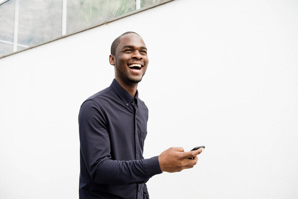 Portrait d'homme afro-américain heureux avec téléphone portable par mur blanc - Photo, image