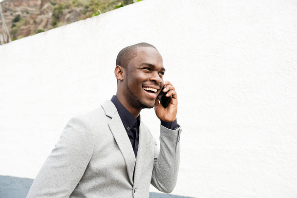 Seitenporträt eines glücklichen afroamerikanischen Geschäftsmannes, der draußen mit dem Handy spricht - Foto, Bild