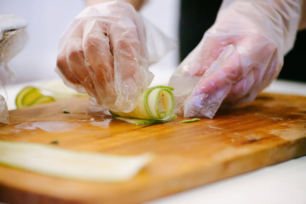 Hands in single use plastic gloves making a roll out of thin cucumber slice - Foto, Bild