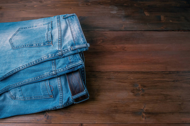Pantalones vaqueros azules sobre un fondo de madera marrón. Pantalones vaqueros deshilachados sobre una superficie de madera áspera. - Foto, imagen