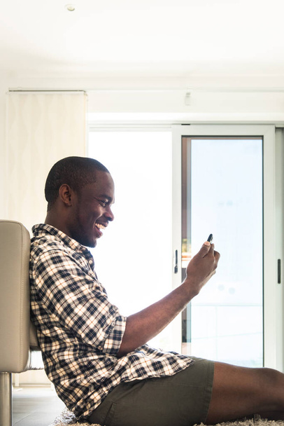 Cep telefonuyla yerde oturan mutlu Afro-Amerikan adam. - Fotoğraf, Görsel