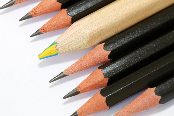 Lápiz grueso multicolor en medio de un grupo de lápices finos y negros alineados, que caracterizan la diferencia y la diversidad
 - Foto, imagen