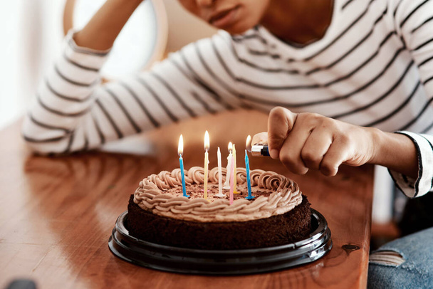 Cumpleaños en cuarentena... no está bien. Recortado disparo de una mujer encendiendo velas en un pastel de cumpleaños en casa y mirando triste. - Foto, Imagen