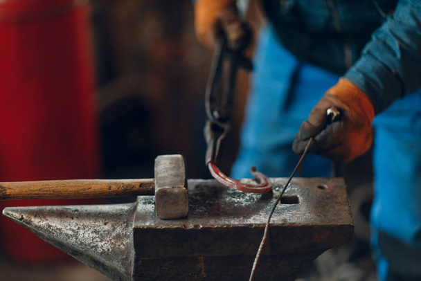 A kovács kovácsol és készít fémrészleteket kalapáccsal és üllővel a kovácsműhelyben - Fotó, kép
