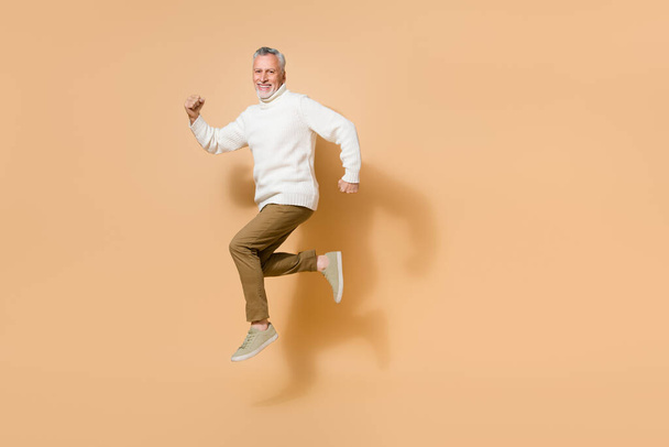 Full length body size view of attractive cheerful man jumping running fast isolated on beige pastel color background - Foto, Imagem