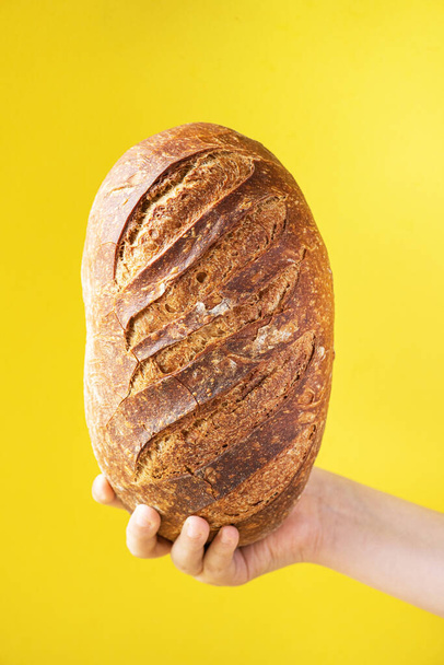 Homemade artisanal sourdough bread in a hand, yellow background. Healthy home baking concept. - Фото, зображення