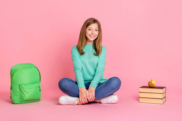 Photo of dreamy school girl dressed teal pullover sitting floor legs crossed isolated pink color background - Foto, Bild