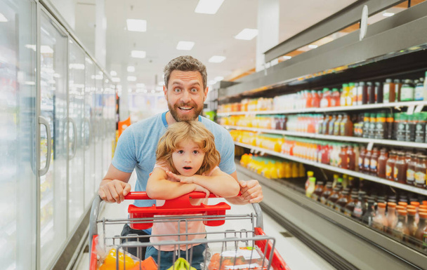 Happy smiling father and child son with shopping cart buying food at grocery store or supermarket. - Foto, immagini