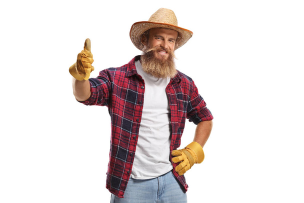 Young farmer with gloves and a straw hat showing thumbs up isolated on white background - Фото, изображение