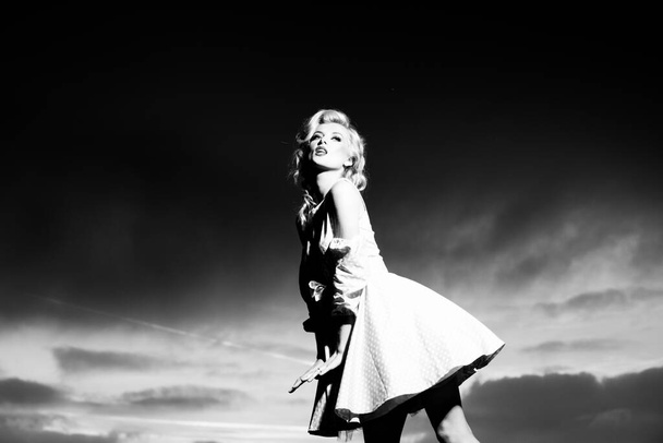 Woman in monroe dress on dramatic sky. Female model in a fashion dress outdoor. - Foto, Imagen