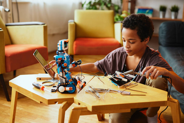 Egy afro-amerikai fiú robotot készít otthon. Otthon a robotika oktatása. - Fotó, kép