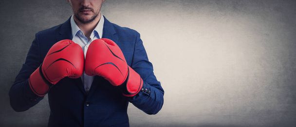 Close up businessman in suit with red boxing gloves stands ready in a fighting stance, punching his fists. Business person self defence concept, isolated on grey wall with copy space. - Photo, Image