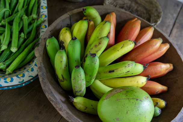 農家では、素朴な木製のテーブルの上にバナナとオクラの束を持つさまざまな材料のボウル。ブラジル・サンパウロ州の田舎 - 写真・画像