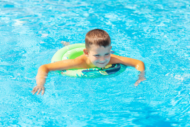 Zabawny szczęśliwy chłopiec w basenie na nadmuchiwanym gumowym kółku. Dzieciak gra w bilard. Wakacje letnie i koncepcja wakacji. - Zdjęcie, obraz