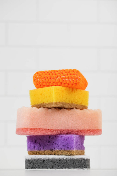 Multicolored sponges for washing dishes are stacked on a white tiled background. - Fotoğraf, Görsel
