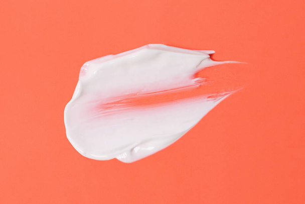 Rozmaz białego kremu kosmetycznego na pomarańczowym tle, forma abstrakcyjna. - Zdjęcie, obraz