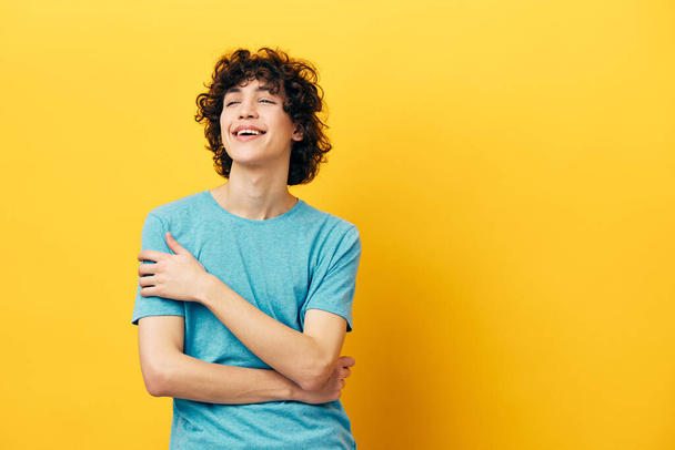 funny curly guy in a blue t-shirt on a yellow background studio - Foto, Imagem