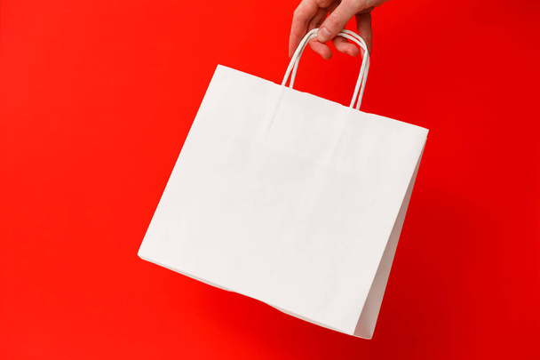 Жіноча рука тримає білу порожню сумку для покупок ізольовано на червоному тлі. Чорна п'ятниця продаж, знижки, переробка, покупки та екологічна концепція
 - Фото, зображення