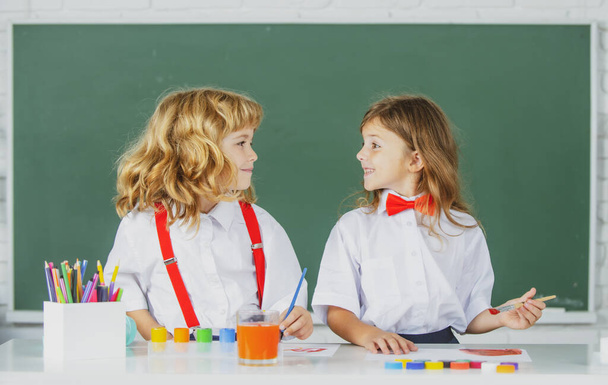 Children doing school lesson at class. Funny school girl an boy pupil drawing a picture. Cute little preschoolers drawing at school. School friends. - 写真・画像