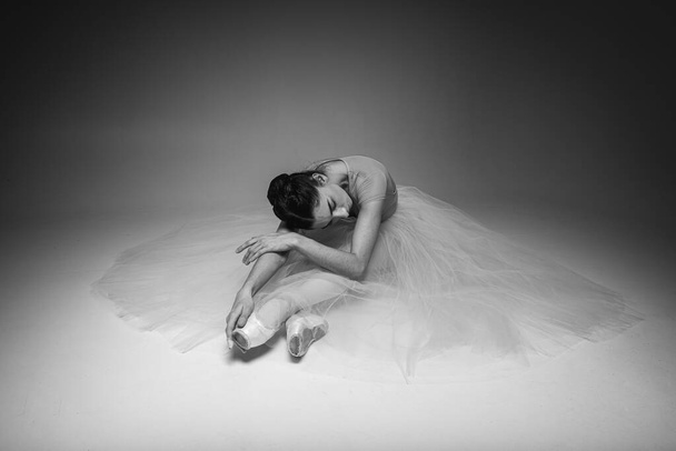 Tired pretty, emotional ballerina sitting on light background background, place for inscription. Black and white photo - Fotoğraf, Görsel
