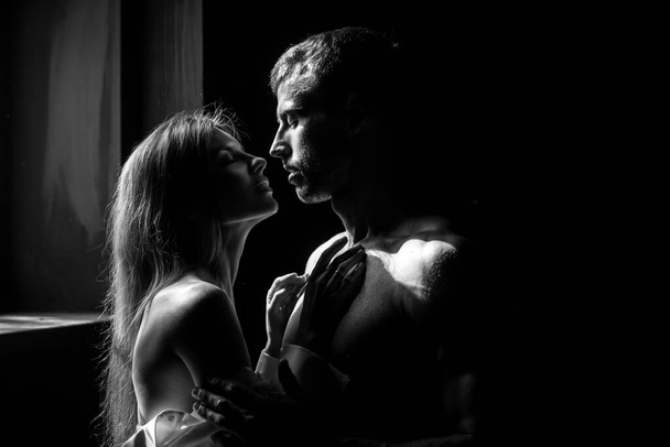 Man embracing and going to kiss sensual woman. Loving couple kissing in bedroom over black background. Real love on Valentines Day. - Фото, изображение