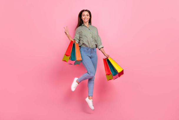 Full size photo of cute young brunette lady jump with bags wear outfit jeans sneakers isolated on pink background - Fotografie, Obrázek