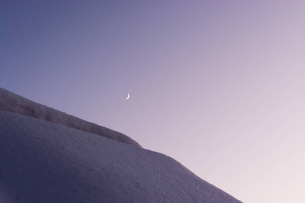 Luna en el cielo sobre un techo cubierto de nieve en una noche de invierno - Foto, Imagen