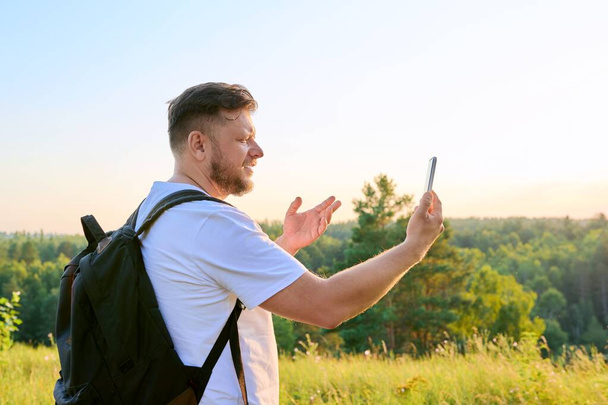 Middle aged bearded man with smartphone backpack on hike, making video call - Photo, image