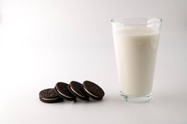 A row of chocolate cream cookies next to glass full of milk on an isolated white background. - Photo, Image