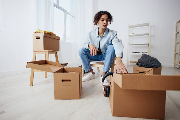 guy with curly hair sitting on a chair with boxes moving sorting things out - Foto, afbeelding