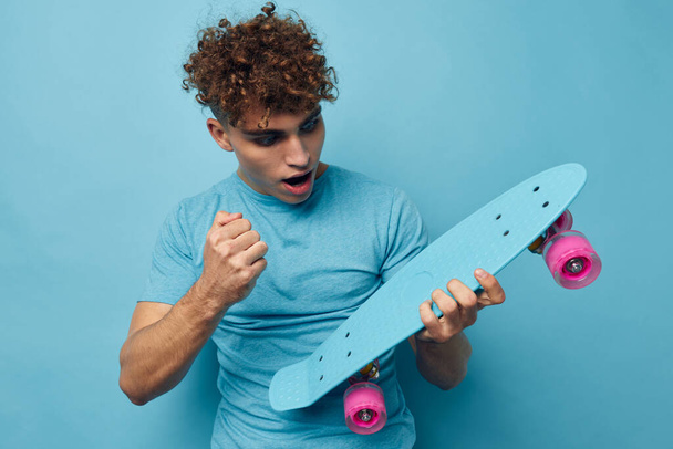 Attractive man skateboard in hand in blue t-shirts blue background - 写真・画像