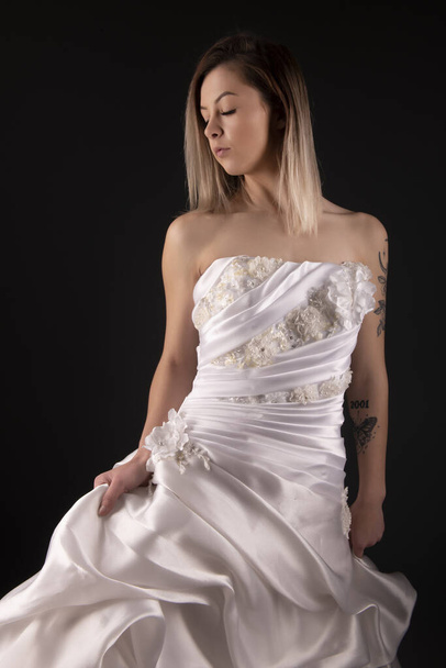 Σέξι νυφικό της νύφης. Μια γυναίκα βγάζει το λευκό φόρεμα. Πίσω όψη κυρία πάνω από μαύρο φόντο. Νυφική μόδα - Φωτογραφία, εικόνα