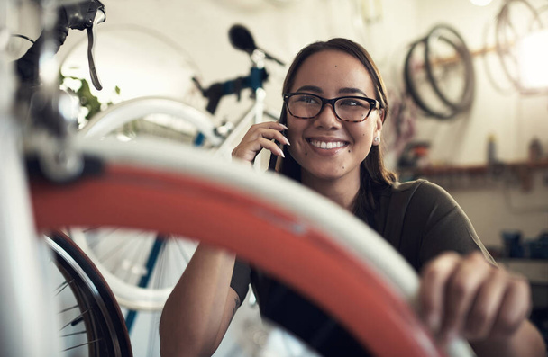 Звоню, чтобы убедиться, что мы получили ваш велосипед. Снимок привлекательной молодой женщины, присевшей в велосипедном магазине и пользующейся телефоном. - Фото, изображение
