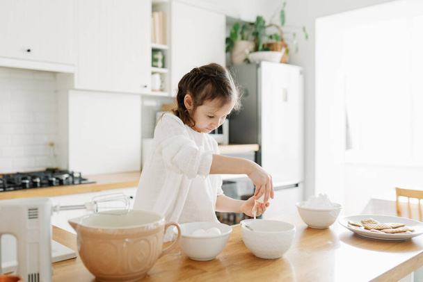 Little Caucasian brown-haired girl baking on white kitchen at home - Foto, Imagem