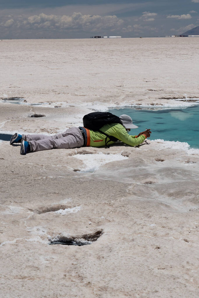 primer plano de una niña con un sombrero de sol tomando fotos con su teléfono celular, frente a un lago donde todo se refleja y el agua se evapora para formar sal. - Foto, imagen