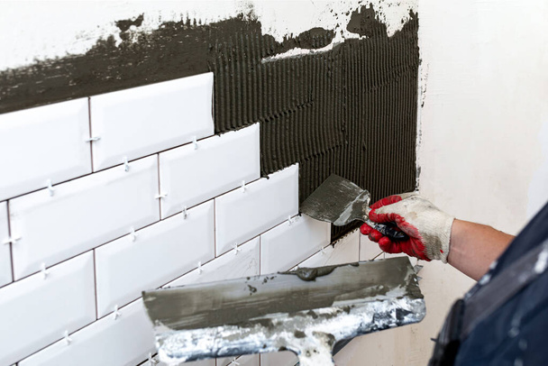 Облицовка стен. Руки мастера приклеивают плитку к стенам двумя лопатками или лопатками разных размеров. Селективный фокус - Фото, изображение