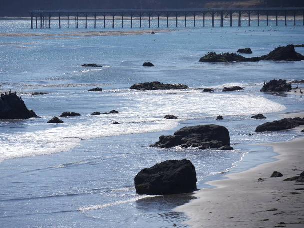 Schuimende golven rollen zachtjes naar de rotsachtige kust van een strand - Foto, afbeelding