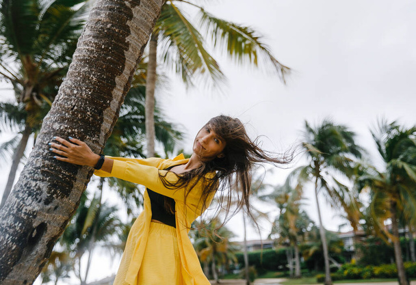 Sarı takım elbiseli güzel, sıska bir esmer kız Dominik Cumhuriyeti 'ndeki bir golf kulübünde tropik palmiye ağaçlarının yanında poz veriyor. - Fotoğraf, Görsel