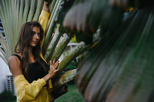 een mooi mager brunette meisje in een geel pak poseert op vakantie in de buurt van tropische palmbomen bij een golfclub in de Dominicaanse Republiek - Foto, afbeelding