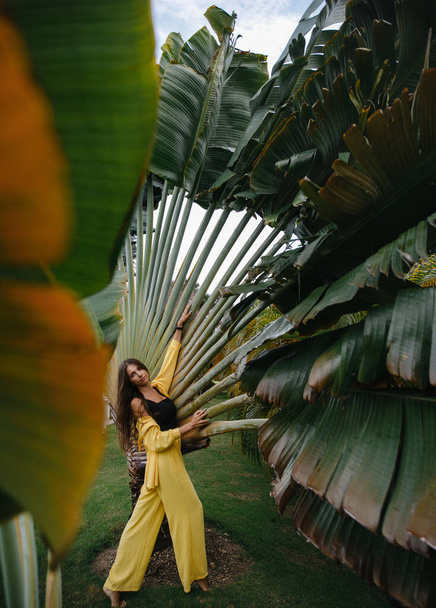 a beautiful skinny brunette girl in a yellow suit poses on vacation near tropical palm trees at a golf club in the Dominican Republic - Photo, image
