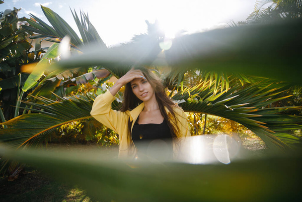 a beautiful skinny brunette girl in a yellow suit poses on vacation near tropical palm trees at a golf club in the Dominican Republic - Φωτογραφία, εικόνα
