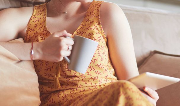 Young woman uses tablet while relaxing at home with coffee on the sofa couch - Foto, immagini