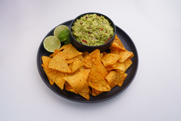 Top view of black plate of guacamole sauce or dip and tortilla chips or nachos isolated on a white background - Foto, Bild