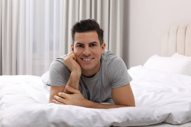 Happy man lying on bed at home - Фото, изображение